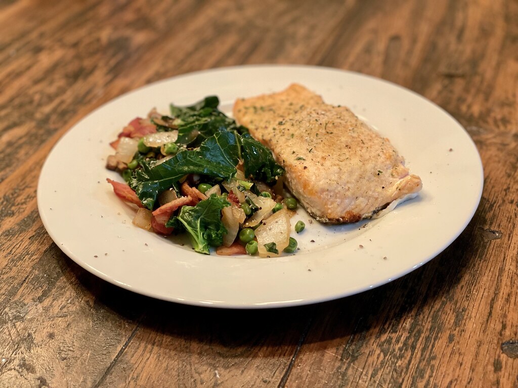 A simple dinner plate of baked fish beside sauteed greens on a wooden table