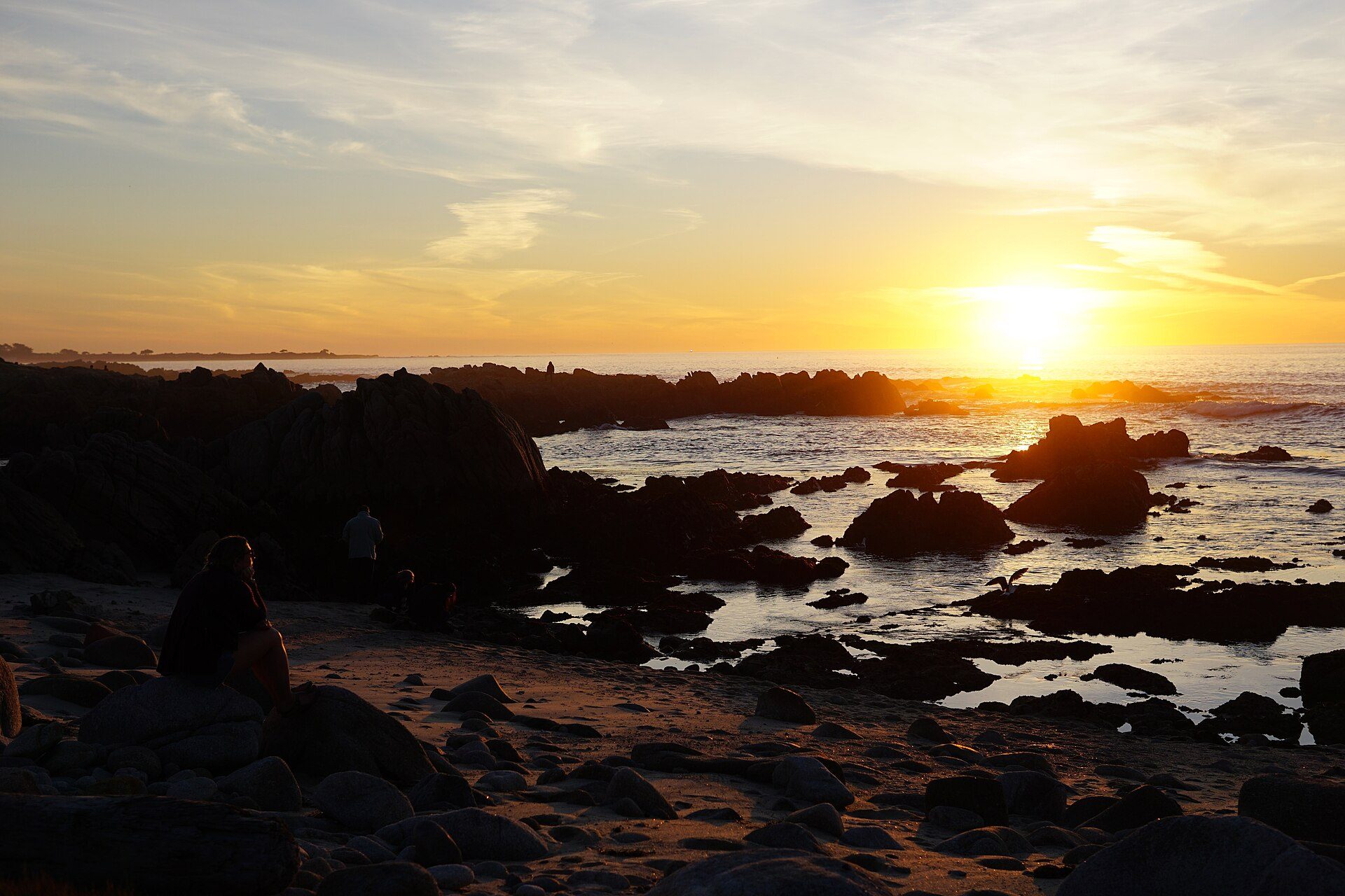 The sun setting over tide pools and wet sand at Asilomar State Beach near Monterey