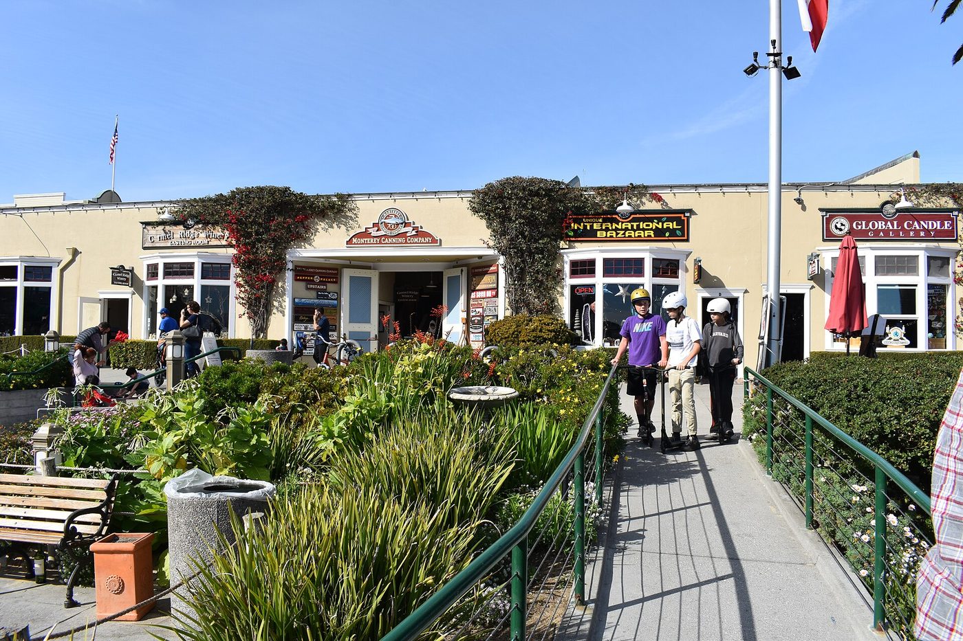 Storefronts, flowers, and families walking along Cannery Row in Monterey on a clear day